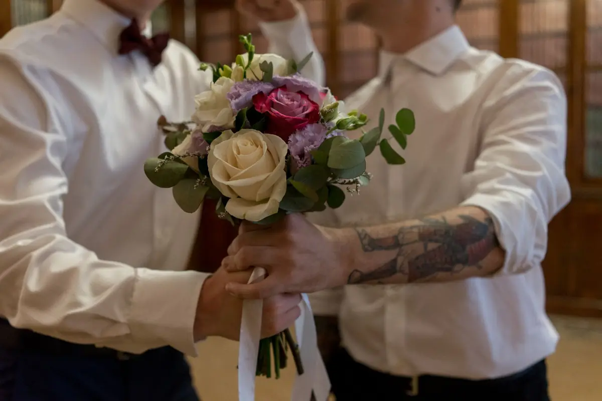 Zwei Bräutigame halten gemeinsam einen Brautstrauß aus weißen Rosen.